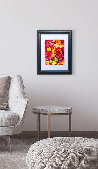 Framed colorful abstract art piece on a wall above a round marble table in a living room.